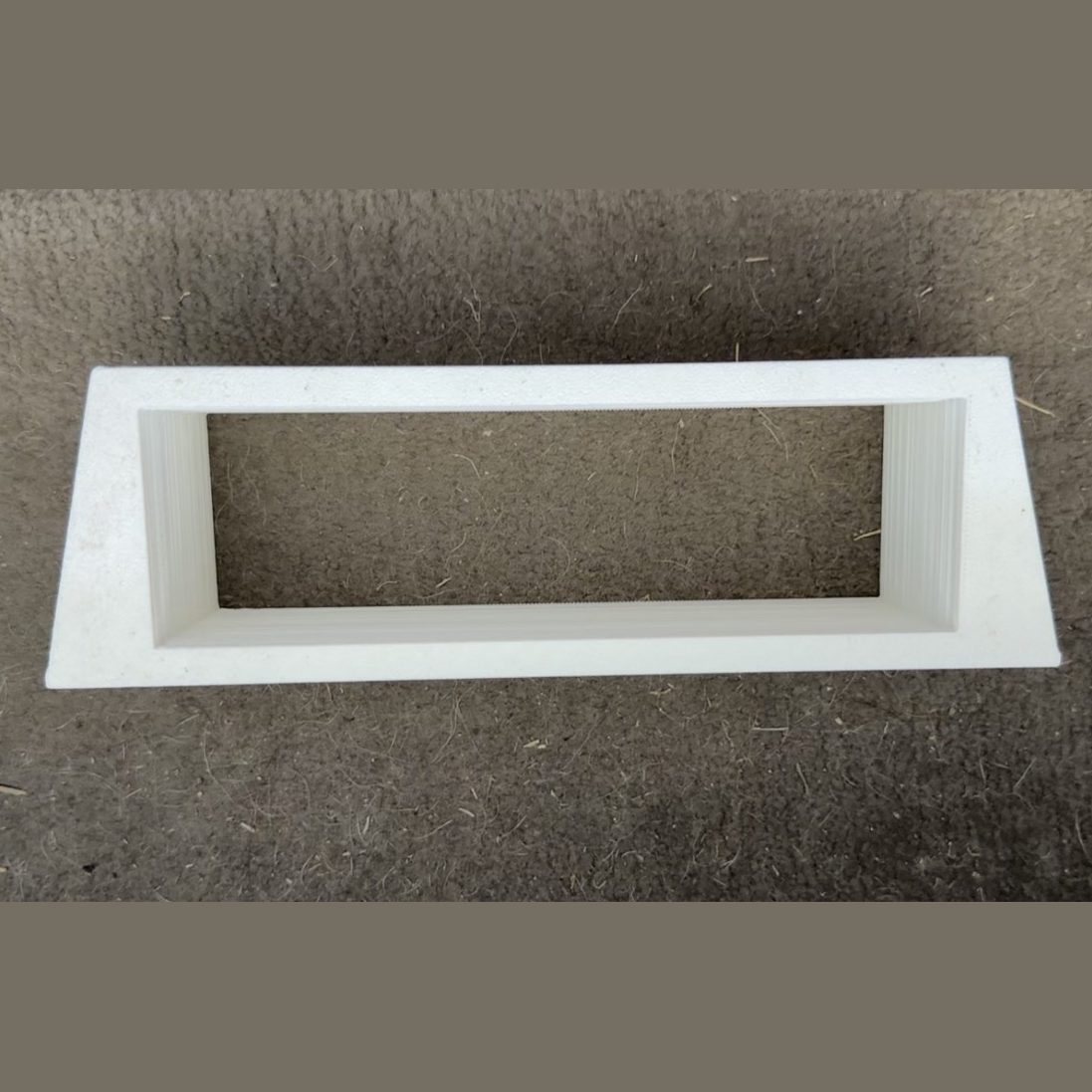White 3D printed trapezoid trim surround bezel lying on carpet